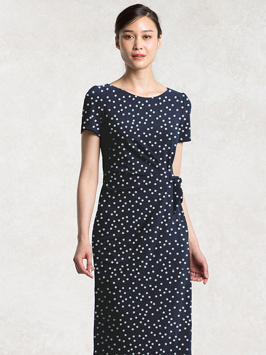 Navy Dot Daily Dress: A woman wearing a navy blue dress with white polka dots, featuring a V-neck and short sleeves.